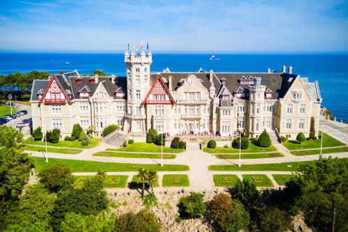 Majestuoso hotel de estilo castillo en Santander frente al azul Mediterráneo, con jardines cuidados y techos rojos