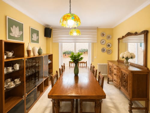 Elegante comedor de la casita de Baiona con paredes amarillas, muebles de madera, lámparas colgantes de vidriera y acceso a vistas al mar
