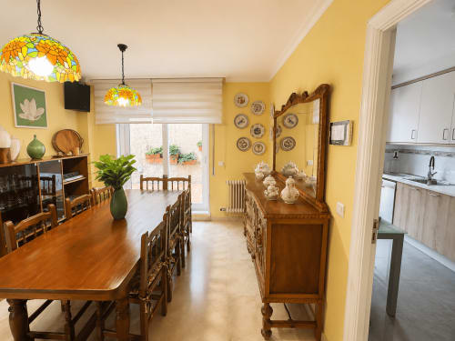 Comedor luminoso en amarillo brillante con muebles de madera, lámparas de vidrio emplomado y acceso a la cocina en la casita Alborada de Baiona