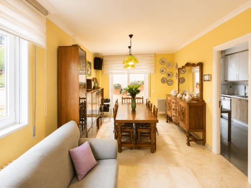 Comedor luminoso en amarillo brillante con muebles de madera, vistas al mar y acceso a cocina en la casa rural de Baiona