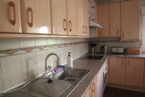 Zona de cocina en Hostal Rosa - Nonna en Sigüenza con muebles de madera, azulejos en la pared y fregadero de acero inoxidable
