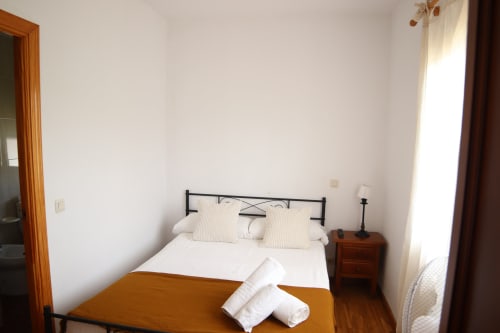 Habitación minimalista y luminosa en Hostal Rosa - Nonna de Sigüenza con cama, mesita de noche de madera y luz natural