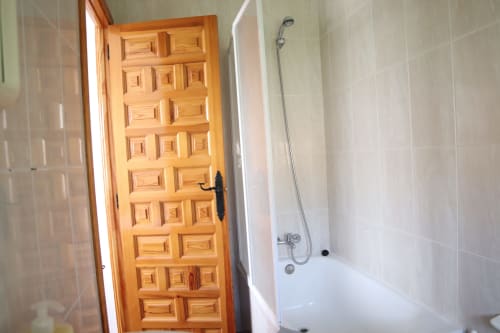 Baño del Hostal Rosa - Nonna en Sigüenza con puerta de madera, azulejos blancos y bañera con ducha.
