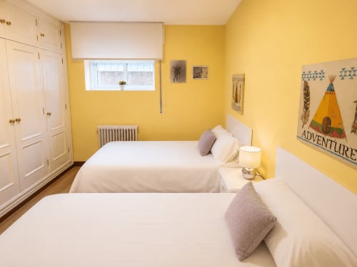 Dormitorio amarillo luminoso con dos camas, armarios blancos y vistas al mar en la casa Holibai de Baiona