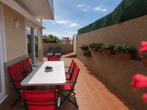 Terraza soleada de la casa Alborada en Baiona con muebles rojos, mesa de comedor y vistas al mar