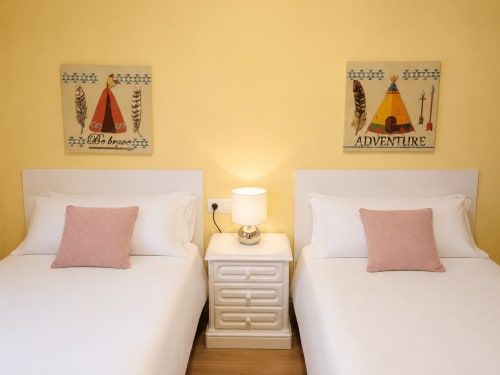 Dos camas gemelas con cabeceros blancos, cojines rosa y decoración náutica en la habitación de la casita Baiona