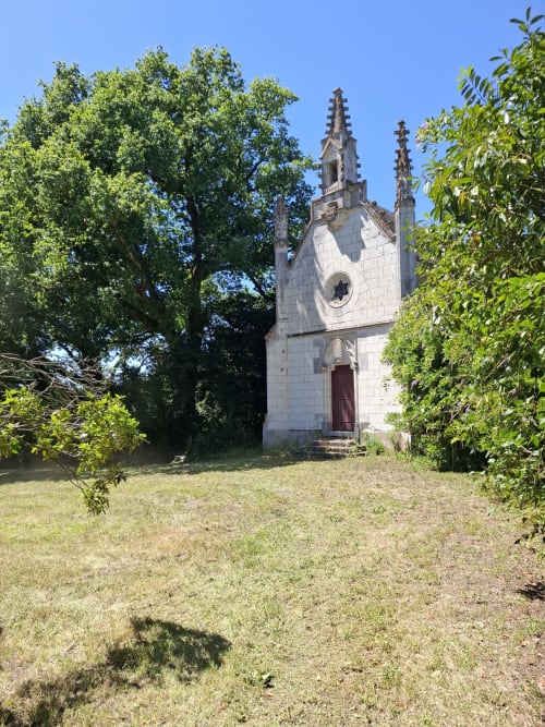Chapelle historique en pierre blanche avec des clochers ornés, entourée d'une verdure luxuriante au Château de Saint Thomas