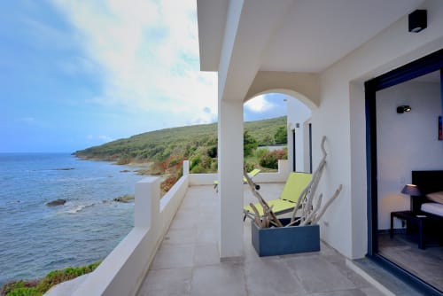 Terrasse de la Villa EOLE avec transat vert anis, vue sur la côte de Centuri, portique blanc dominant les eaux méditerranéennes et