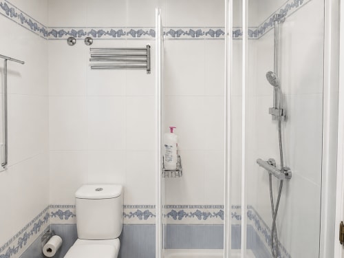 Baño moderno con azulejos blancos, cenefa decorativa azul, ducha abierta, inodoro y herrajes cromados en la cabaña Holibai