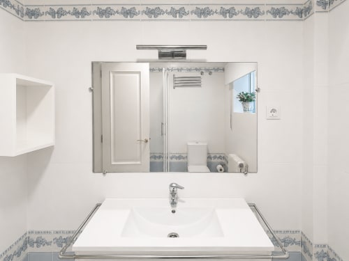 Lavabo moderno y espejo en la casa rural Alborada, Baiona. Acentos de azulejos azules, tocador blanco, grifería cromada.
