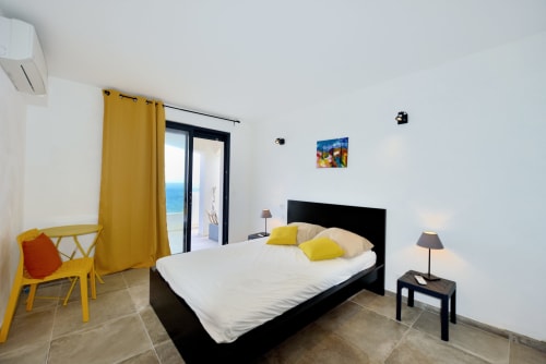 Chambre moderne de la Villa EOLE à La Conciergerie du Cap Corse avec vue mer, lit noir, accents jaunes et balcon à Centuri