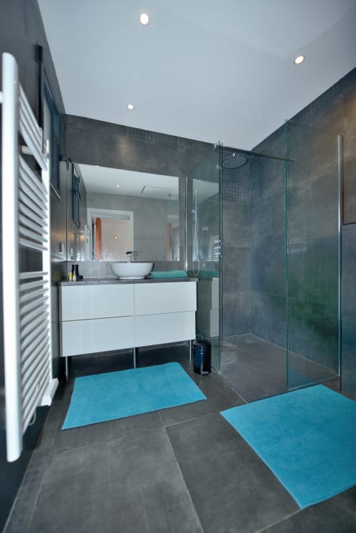 Salle de bains moderne de la Villa EOLE à La Conciergerie du Cap Corse : carrelage noir, vasque blanche, douche à effet pluie et turquoise
