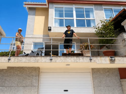 Dos huéspedes en la terraza de la casita Alborada en Baiona con vistas al mar, ventanales modernos y jardín