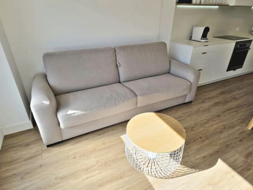 Moderno salón en apartamento BR SILGAR Sanxenxo con sofá beige, mesa auxiliar blanca y suelo de madera