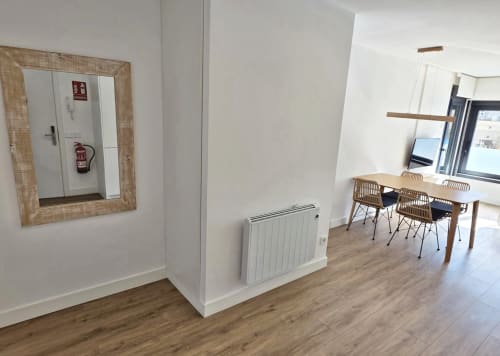 Pasillo moderno del apartamento BR Silgar Sanxenxo con suelos de madera, paredes blancas, radiador, espejo y zona de trabajo con escritorio