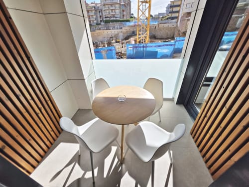 Terraza luminosa del apartamento BR SILGAR Sanxenxo con mesa redonda, sillas blancas y vistas a la ciudad a través de grandes ventanales