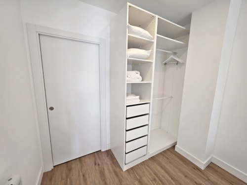 Armario moderno con estanterías blancas, cajones y espacio para colgar en el apartamento BR Silgar de Sanxenxo