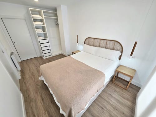 Dormitorio moderno en apartamento BR Silgar Sanxenxo con cama de matrimonio, ropa blanca, cabecero de madera, armario empotrado y acabados en madera