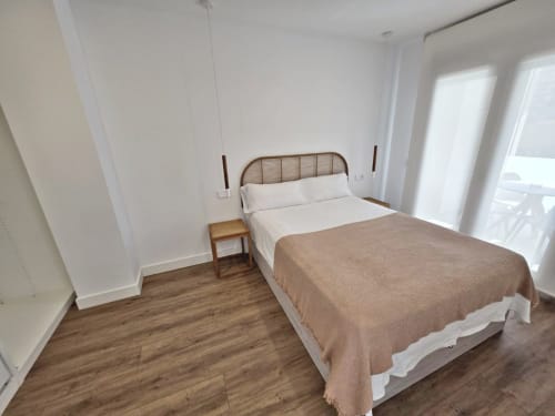 Dormitorio luminoso en BR Silgar Sanxenxo con cama de madera, ropa de cama blanca y puertas de terraza con vistas a la costa