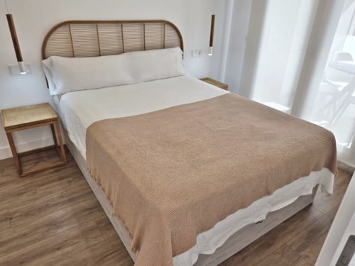 Dormitorio luminoso en BR SILGAR Sanxenxo con cabecero de ratán, ropa de cama beige, mesita de noche de madera y luz natural desde la terraza
