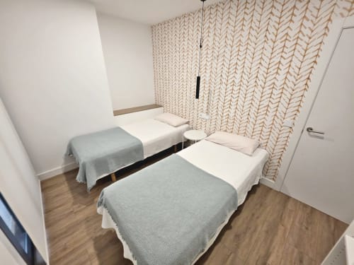 Dormitorio doble en apartamento BR Silgar en Sanxenxo con sábanas blancas, cortinas beige con patrón y suelo de madera