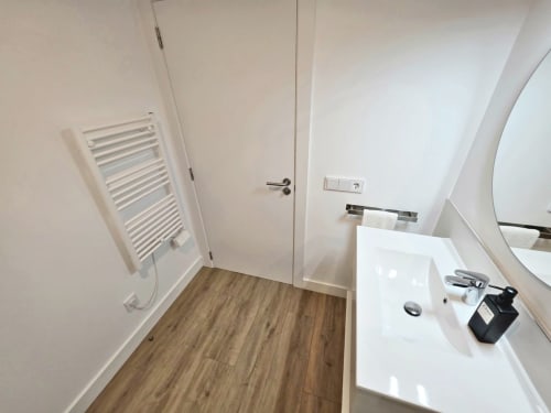 Baño moderno del apartamento BR SILGAR Sanxenxo con lavamanos blanco, toallero calefactor y suelos de madera