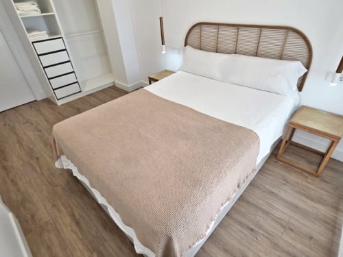 Habitación moderna en BR Silgar Sanxenxo con cama de cabecera de ratán, sábanas blancas, manta beige y mesita de noche de madera