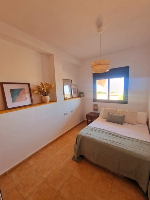 Dormitorio moderno con vistas al mar en Mirador de los Collados, Águilas, con cama, suelos de terracota y ventana de marco azul