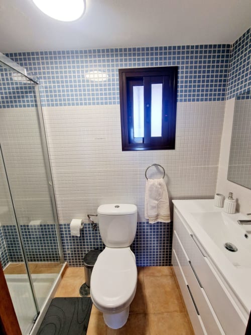 Baño moderno con detalles de azulejos azules, accesorios blancos y ducha en ATTC International Vacaciones en Águilas, España