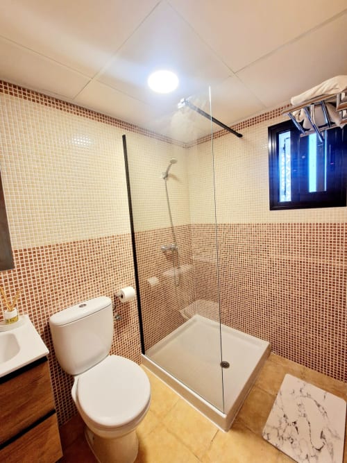 Baño moderno con paredes de azulejos mosaico, cabina de ducha de cristal e inodoro en ATTC International vacaciones en Águilas