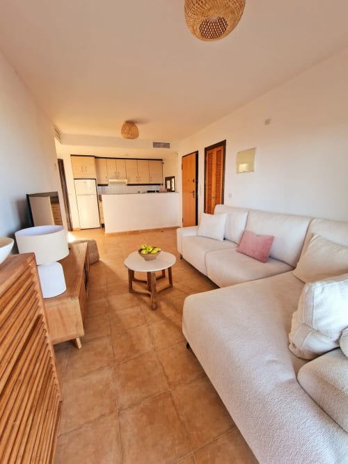 Luminosa sala de estar con sofás beige, muebles de madera y cocina en la casa vacacional ATTC Aguilas