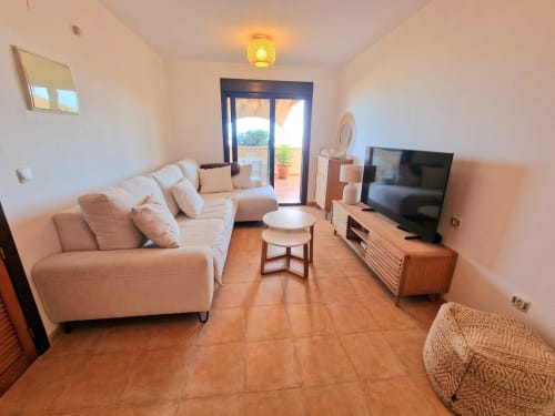 Luminosa sala de estar con sofá beige, televisor y balcón con vista al mar en Mirador de los Collados, Águilas