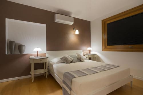 Camera moderna presso Country Domos B&B a Ozieri con letto beige, parete d'accento marrone, pavimenti in legno e vista sul giardino