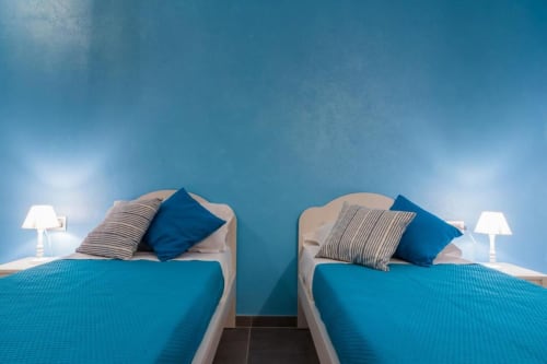 Due letti gemelli con biancheria blu nella Blue Room di Country Domos B&B a Ozieri, Italia, con pareti turchesi e giardino