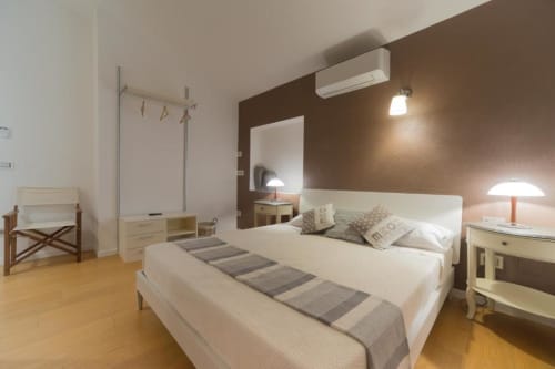 Camera da letto moderna presso Country Domos Ozieri con letto bianco, parete accent marrone, pavimenti in legno e vista giardino