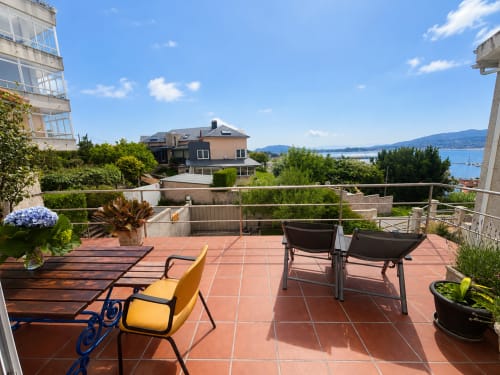 Terraza soleada con sillas coloridas, vista al mar y montañas en la casita Holibai de Baiona, España
