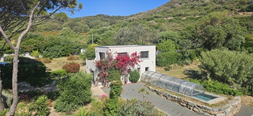 Villa EOLE aux façades blanches, bougainvillées magenta en fleurs, piscine couverte dans un jardin luxuriant de Centuri