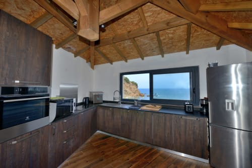 Cuisine de villa moderne avec électroménagers en acier inoxydable, vue mer par grandes baies vitrées, poutres en bois, Corse
