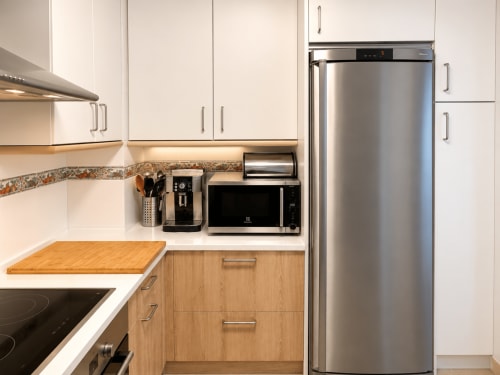 Cocina moderna con electrodomésticos de acero inoxidable, muebles blancos y unidades inferiores de madera en la casa de campo Alborada, Baiona