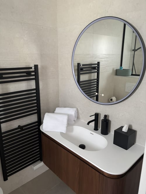 Salle de bains moderne de la résidence Les 3 Volcans avec miroir rond, sanitaires noirs et sèche-serviettes électrique