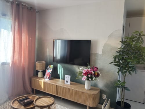 Salon moderne de la Résidence Les 3 Volcans avec télévision, console en bois, rideaux roses, fleurs et plantes décoratives