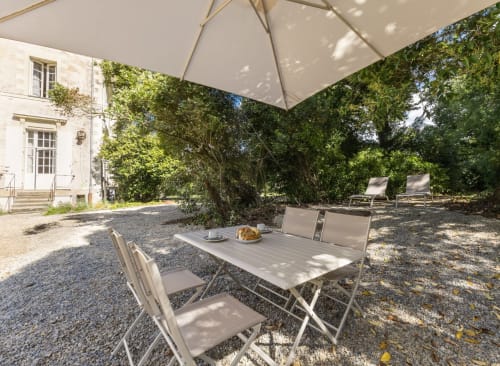 Espace de restauration en plein air au Château de Saint Thomas avec parasols, table et chaises entourés de verdure luxuriante