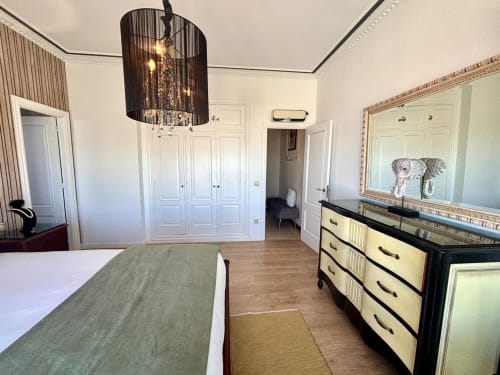 Dormitorio de lujo en la casa Serenidade, Baiona, con elegante lámpara de araña negra, armario blanco, tocador, espejo grande y vistas al mar