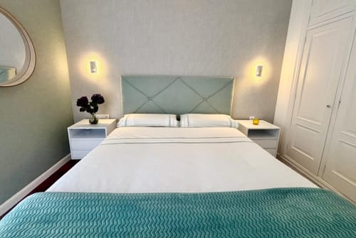 Moderno dormitorio en la cabaña Holibai de Baiona con cama de matrimonio, cabecero salvia, mesitas blancas e iluminación ambiental