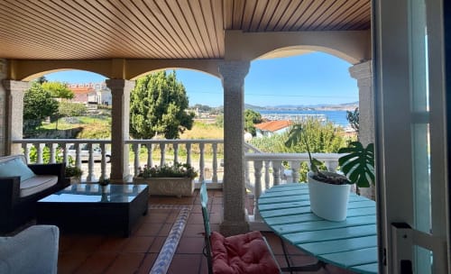 Amplia terraza de la casita Serenidade en Baiona con vistas al mar, zona de descanso y plantas en macetas con vista a la costa
