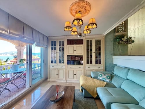 Luminosa sala de estar junto al mar en la casita Holibai Baiona con sofá turquesa, muebles color crema, lámpara ornamental y vistas al océano