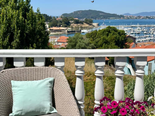 Terraza de la casa Serenidade en Baiona con vistas al mar, silla de mimbre, flores rosas y marina