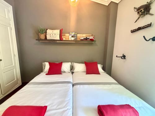 Dormitorio de la cabaña Serenidade en Baiona con camas blancas, almohadas rojas, estantería de madera y decoración temática pirata