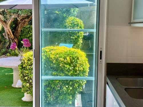 Puertas de cristal con vistas a exuberante jardín con flores amarillas y púrpuras vibrantes, cabaña Holibai en Baiona con vistas al mar