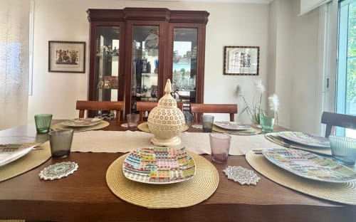 Mesa de comedor elegante en la casa Holibai de Baiona con cubiertos, vistas al mar por las ventanas y muebles de madera oscura.